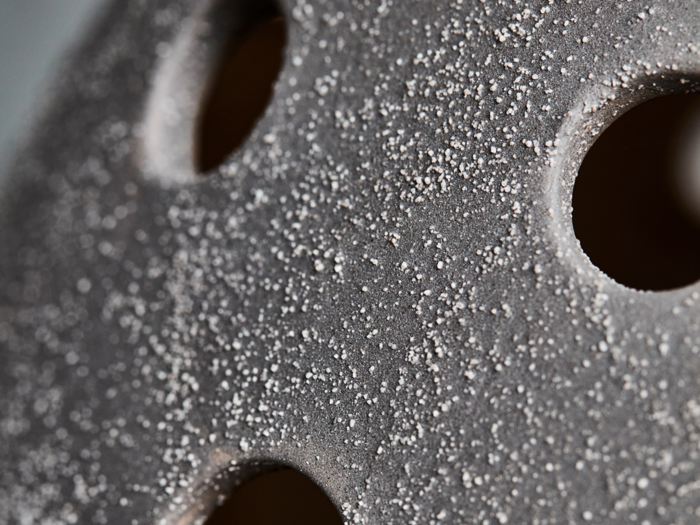 Nærbillede af en ru, grå overflade med små hvide pletter og flere jævnt fordelte runde huller.