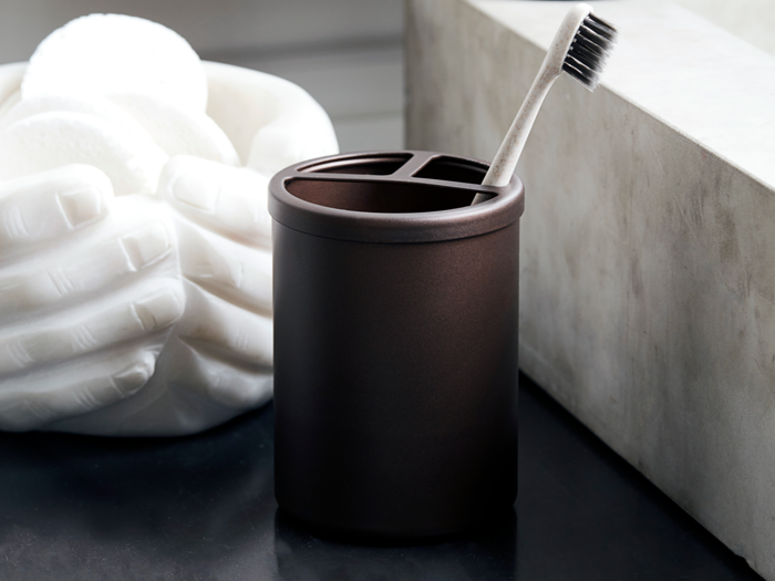 En sort tandbørsteholder med en tandbørste indeni står på en mørk disk ved siden af en hvid skulptur af hænder, der holder runde genstande.