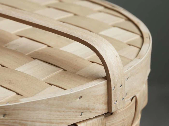 Nærbillede af en flettet trækurv med en buet træhank og synlige metalklammer, der fastgør strimlerne.