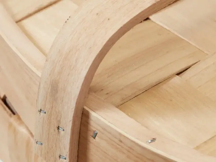 Nærbillede af en trækurv med buet hank og flettede lameller, der viser metalklammer, der fastgør håndtaget til kurven.