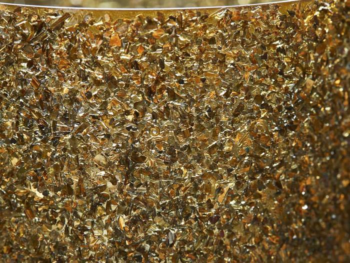 Et nærbillede af mange små, uregelmæssigt formede gyldne fragmenter, der er tæt pakket sammen og skaber en struktureret og skinnende overflade.
