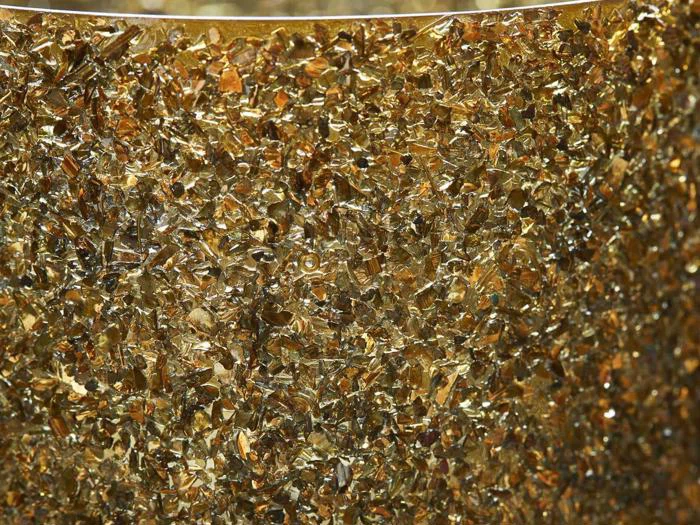 Et nærbillede af mange små, uregelmæssigt formede gyldne fragmenter, der er tæt pakket sammen og skaber en struktureret og skinnende overflade.
