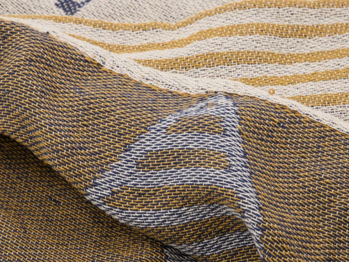 Nærbillede af vævet stof med brune, hvide og blå tråde med geometriske mønstre og striber. Stoffet virker struktureret og let krøllet.