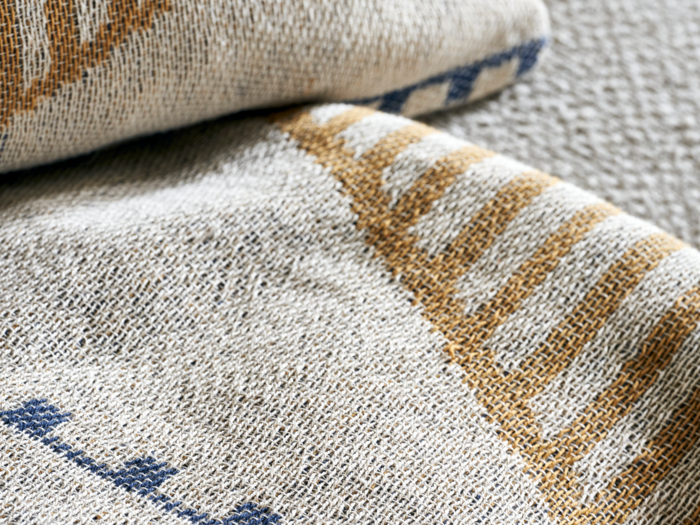 Nærbillede af vævet stof med beige, blå og guldfarvede geometriske mønstre, der viser tekstur og syningsdetaljer.