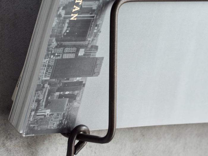 Nærbillede af en bog med et gråtonet bybillede på omslaget, delvist holdt af et bogstativ af metal på en grå overflade.