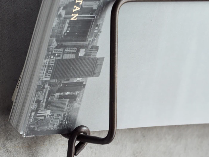 Nærbillede af en bog med et gråtonet bybillede på omslaget, delvist holdt af et bogstativ af metal på en grå overflade.