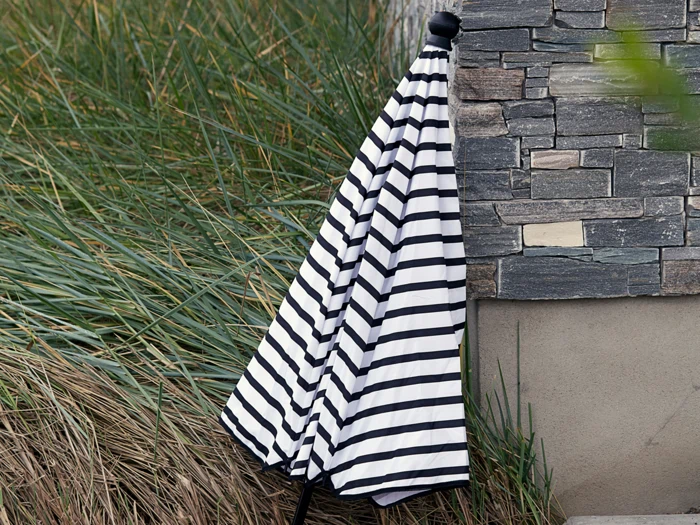 En lukket sort- og hvidstribet paraply står ved siden af en stenmur med højt grønt græs i baggrunden.