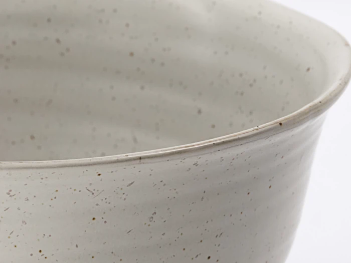 Nærbillede af en lysegrå, spættet keramikskål med en glat, let buet kant mod en almindelig hvid baggrund.