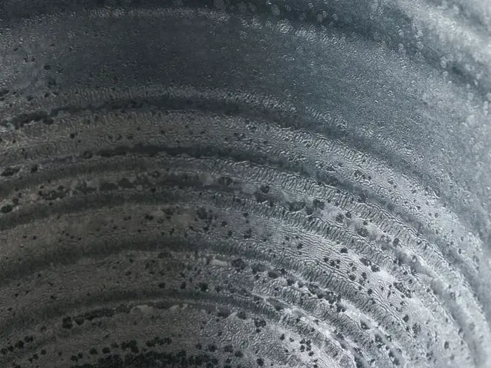 Nærbillede af en metallisk overflade med cirkulære mønstre og små mørke pletter, der ligner ringe eller riller med et struktureret, forvitret udseende.