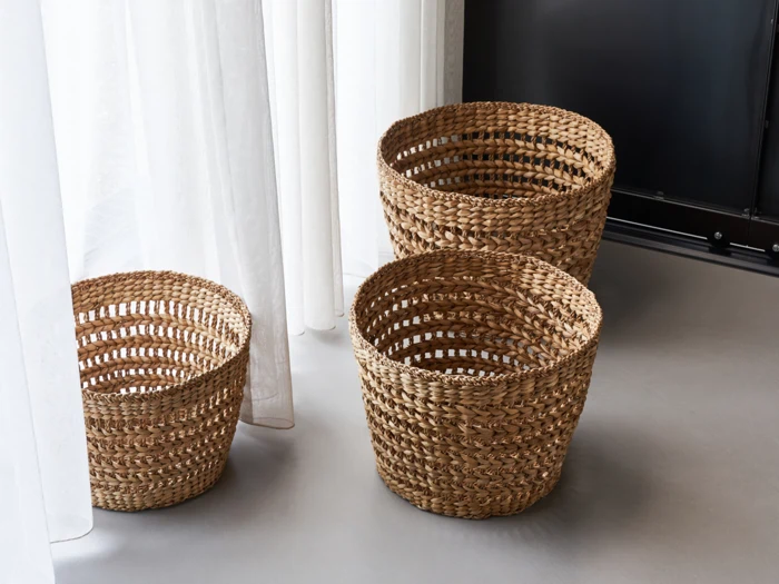 Tre flettede kurve i forskellige størrelser er anbragt på et gråt gulv i nærheden af hvide gardiner og en sort væg.