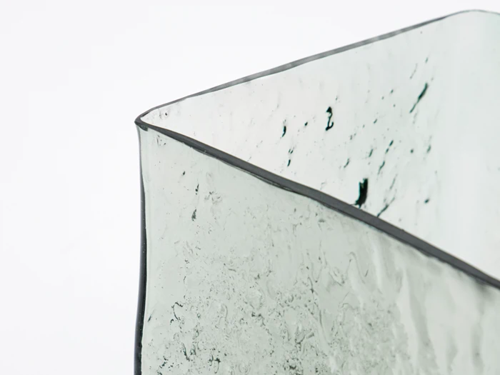 Nærbillede af en gennemsigtig, struktureret glasbeholder med bølgede, ujævne kanter mod en almindelig hvid baggrund.