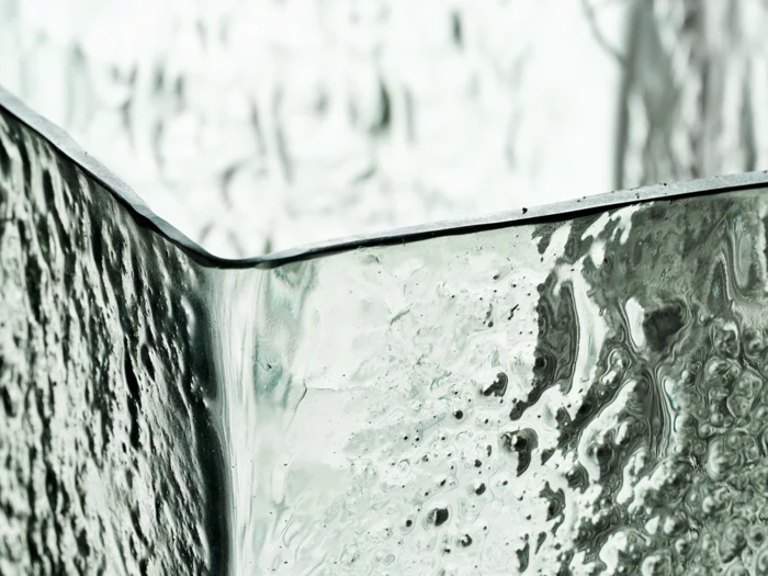 Nærbillede af den strukturerede, gennemskinnelige overflade på et glasobjekt med kantede kanter og et let grønligt skær.
