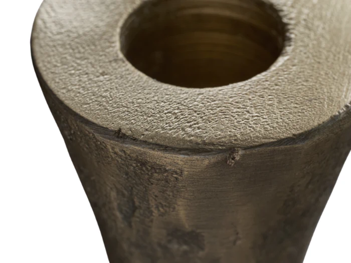 Nærbillede af den øverste kant og åbningen af en grov tekstureret, cylindrisk metalgenstand med en hul midte.