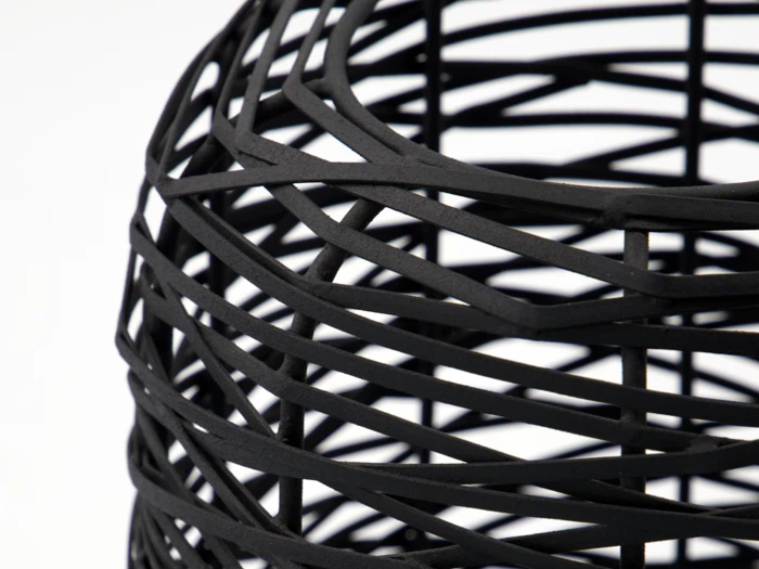 Nærbillede af et moderne, sort, geometrisk wireframe-objekt med overlappende diagonale linjer på en almindelig hvid baggrund.