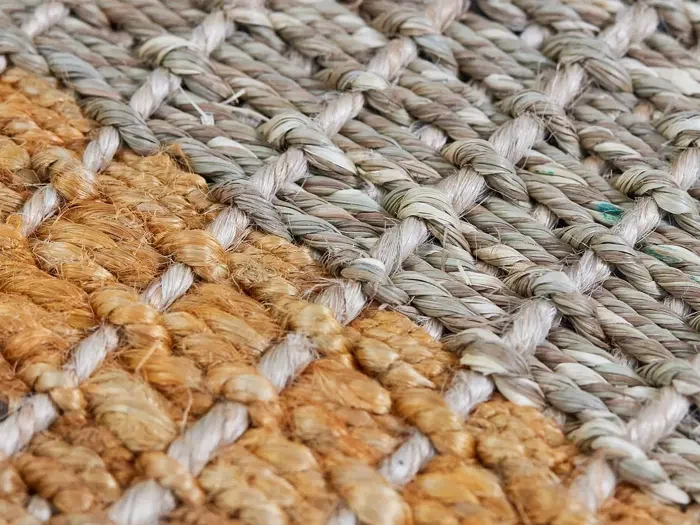 Nærbillede af en vævet måtte med sammenflettede grå og brune fibre, der viser materialets detaljerede struktur og mønster.