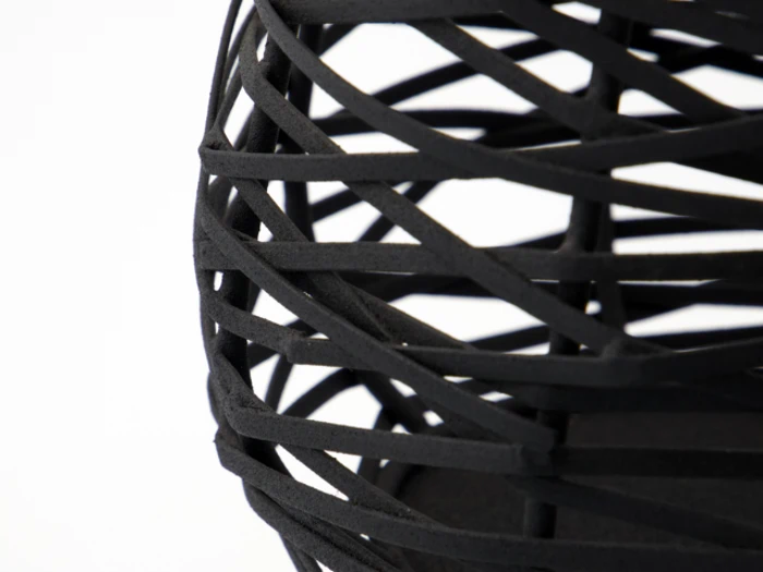 Nærbillede af en sort, åbent vævet, geometrisk struktur med krydsende bånd på en almindelig hvid baggrund.