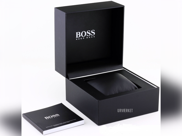 En sort Hugo Boss-urkasse med åbent låg, der viser et polstret rum indeni og et hæfte med påskriften BOSS placeret ved siden af.