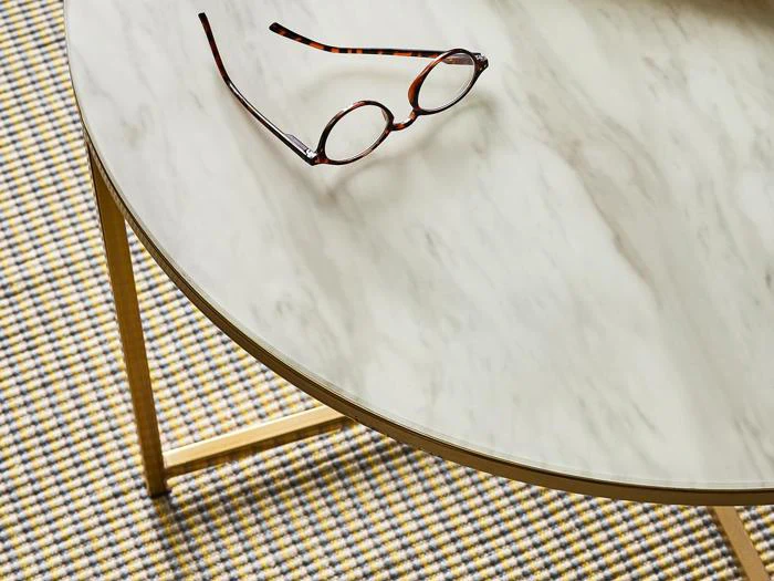 Rundt bord med marmorplade og tynde guldben, hvorpå der hviler et par skildpaddebriller; mønstret tæppe nedenunder.