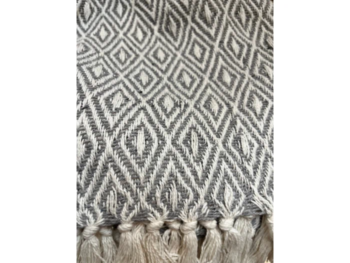 Nærbillede af et vævet stof med et gentagende diamantmønster i sort og hvid, med frynsede kvaster langs den nederste kant.