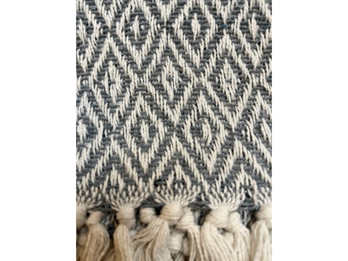 Nærbillede af et vævet stof med et geometrisk diamantmønster i sort og hvid, med en række beige kvaster langs den nederste kant.