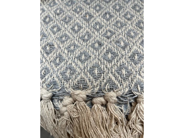 Nærbillede af et vævet stof med diamantmønster i grå og beige toner, med knyttede frynsekvaster langs kanten.