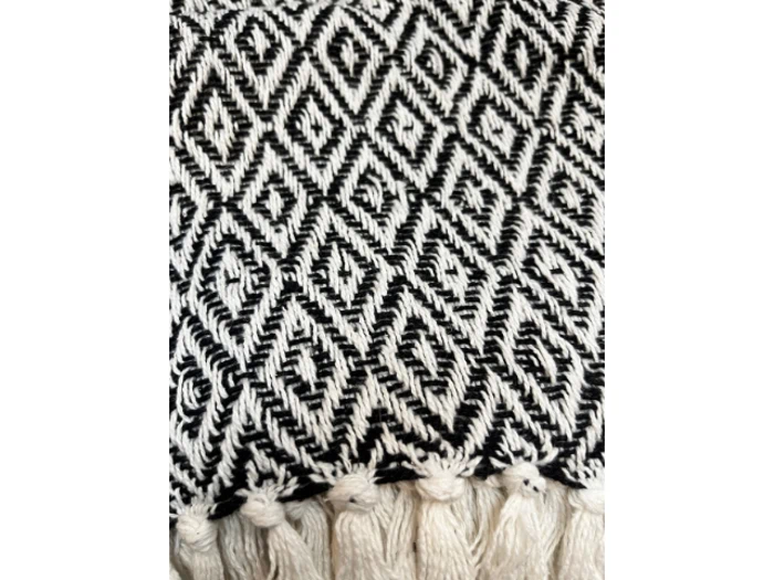 Nærbillede af et vævet tekstil med et sort og hvidt diamantmønster og kvaster langs den nederste kant.