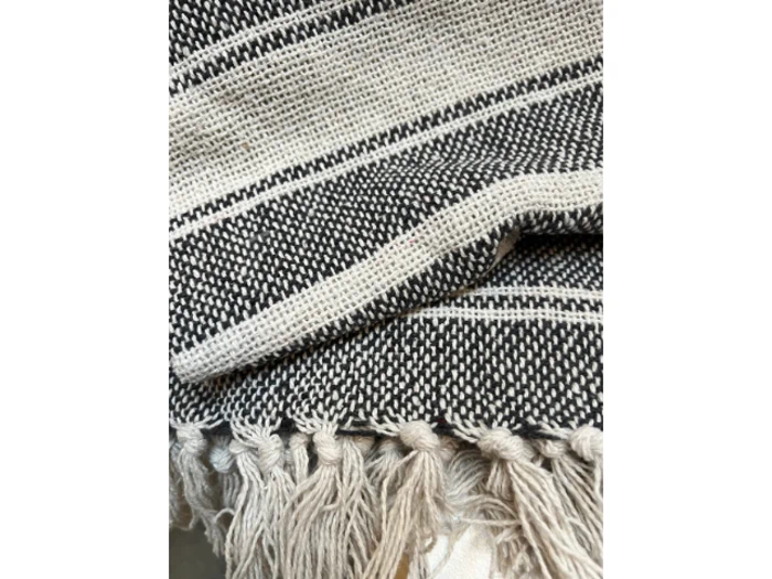 Nærbillede af et vævet sort og hvidt tekstil med frynsede kanter og vandrette striber. Stoffet ser ud til at være struktureret og let foldet.