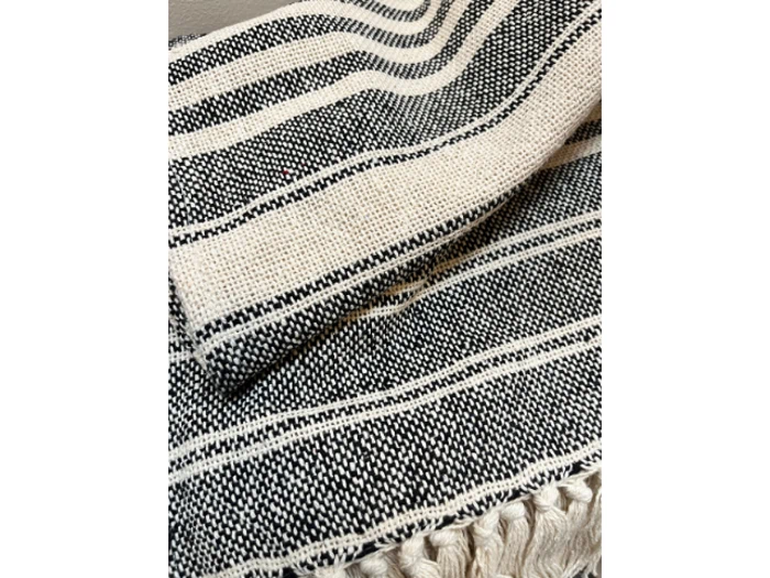 Nærbillede af et sort og hvidt vævet tæppe med vandrette striber og frynser langs kanten.
