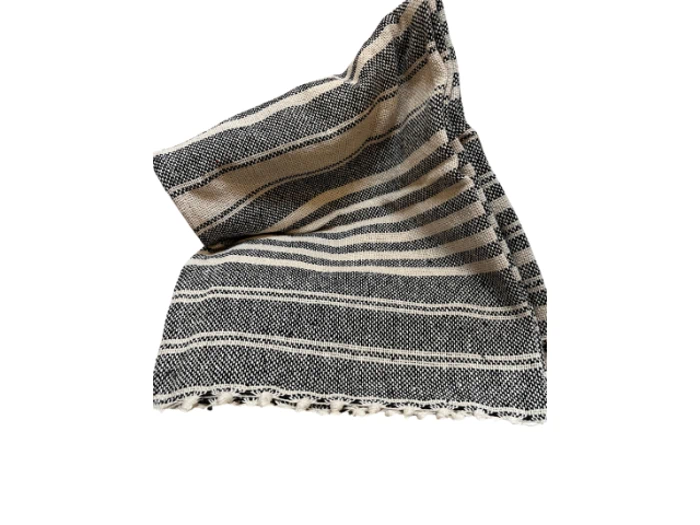 Et foldet, sort- og cremefarvet, stribet vævet tekstil med flossede kanter, vist på en hvid baggrund.