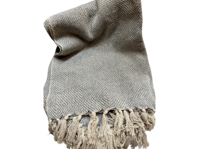 Et gråt tekstureret tæppe med et subtilt diamantmønster og frynsede kvaster langs den ene kant, spredt ud mod en hvid baggrund.