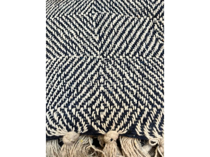 Nærbillede af et vævet stof med et sort og beige geometrisk zigzagmønster og kvastede frynser i bunden.