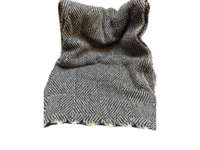 Et sort og hvidt sildebensmønstret tørklæde eller stof, let krøllet, med ufærdige frynsekanter forneden, på en hvid baggrund.