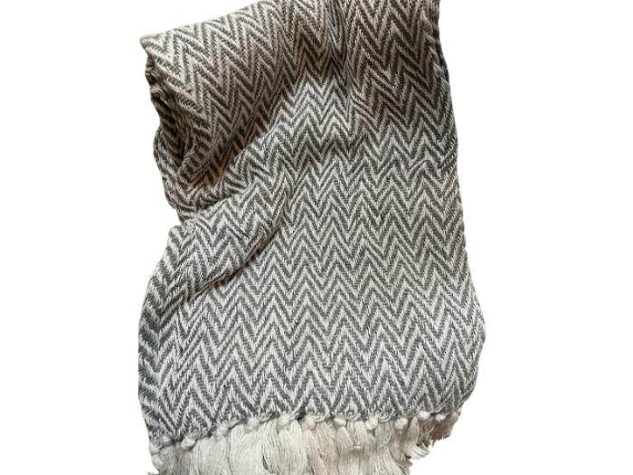 Et foldet gråt og hvidt chevronmønstret tæppe med frynsede kanter, isoleret på en hvid baggrund.