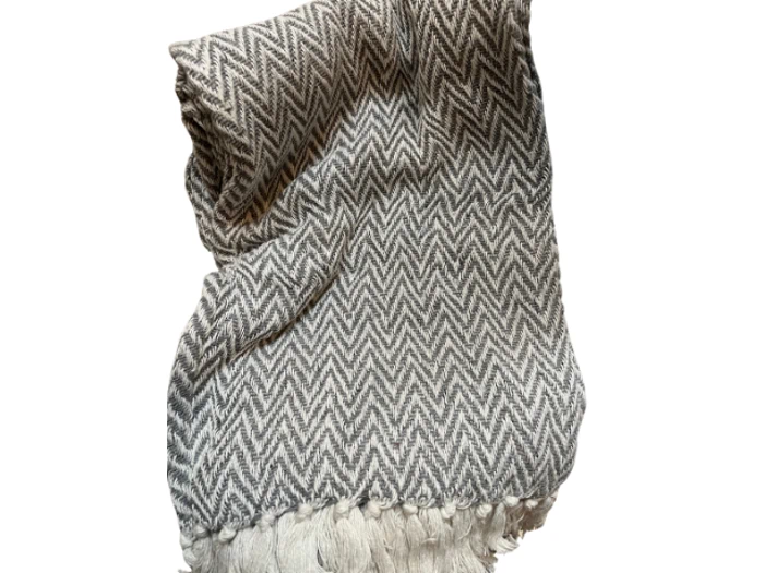Et foldet gråt og hvidt chevronmønstret tæppe med frynsede kanter, isoleret på en hvid baggrund.