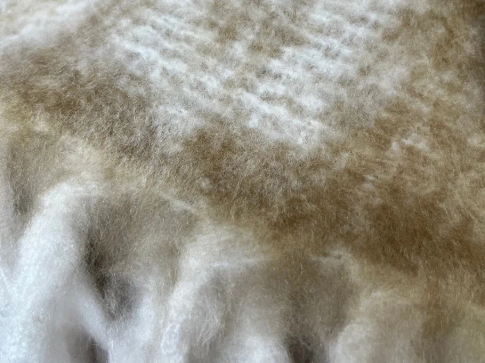 Nærbillede af et blødt, loddent beige og hvidt stof, muligvis uld eller et tæppe, som viser dets bløde tekstur og blide farvegraduering.