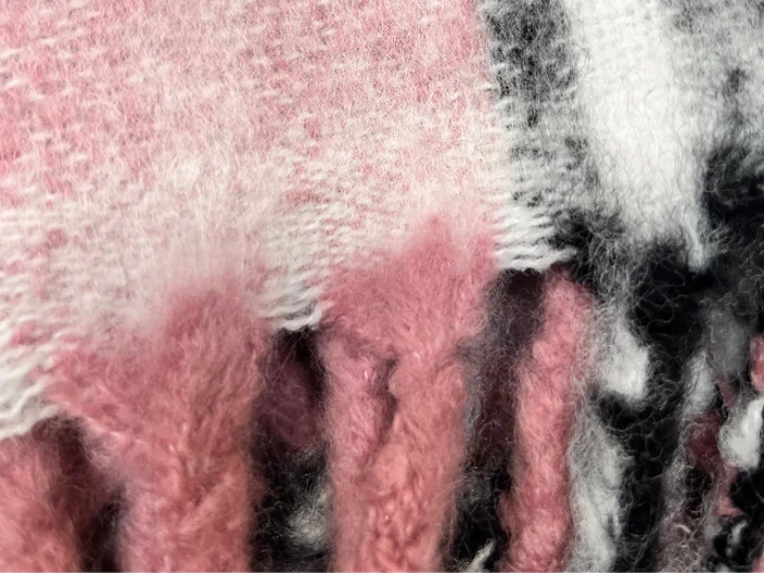 Et nærbillede af et blødt, luftigt stof med rosa, hvide og sorte farver, der blander sig med hinanden, og som viser strukturerede fibre og frynsede kanter.