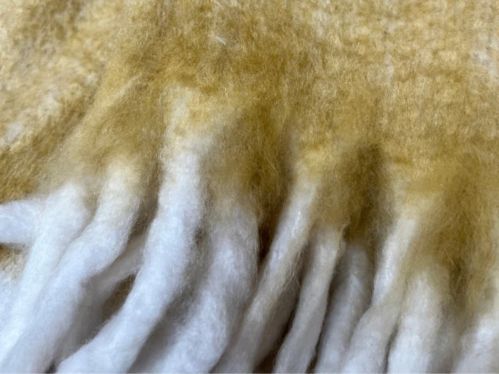 Nærbillede af bløde, fluffy hvide og lysebrune fibre, der ligner teksturen i et uld- eller fleecestof.