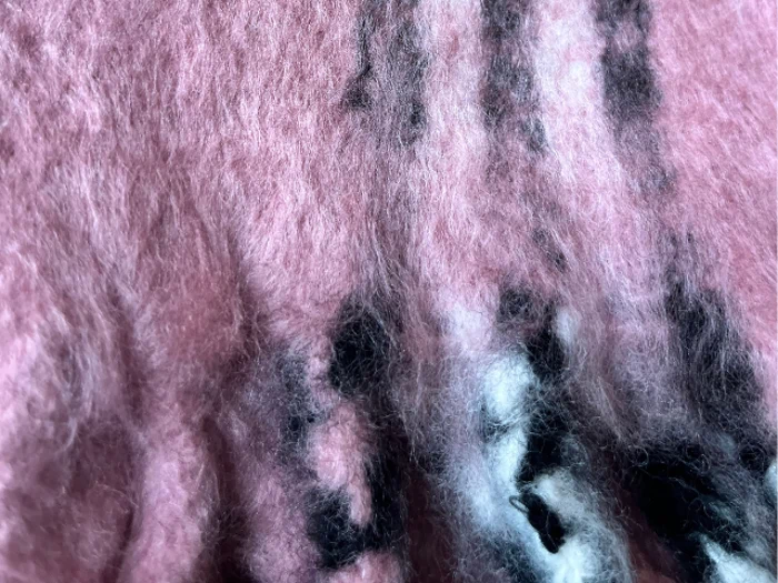 Nærbillede af et lyserødt, loddent stof med nogle sorte og hvide striber eller mønstre, der løber igennem det.