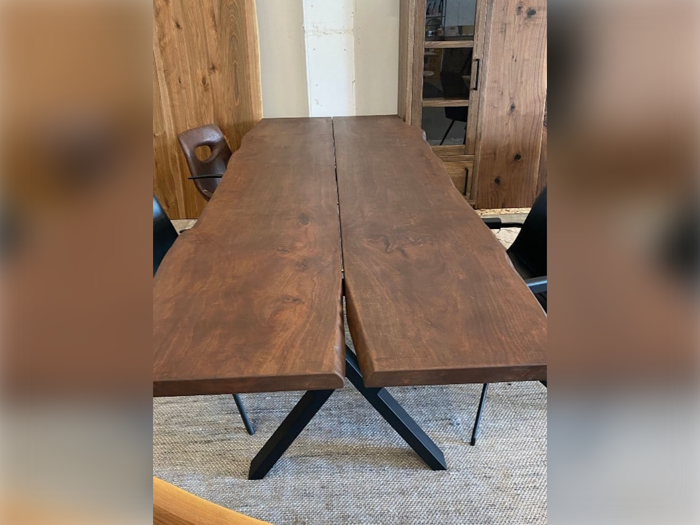 Et spisebord i træ med en naturlig flænge i midten, sorte metalben og sorte stole omkring det, placeret på et beige tæppe.