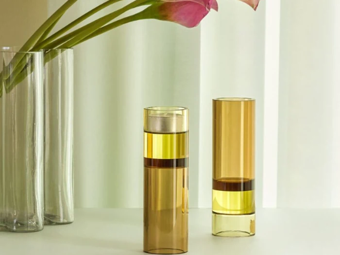 To ravfarvede glasbægre står på en hvid flade ved siden af en høj vase med lyserøde blomster på en lys baggrund.