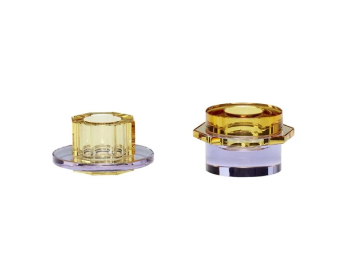 To geometriske, gennemsigtige glaslysestager - en kortere og en højere - begge med gule toppe og lilla baser, vist på en hvid baggrund.