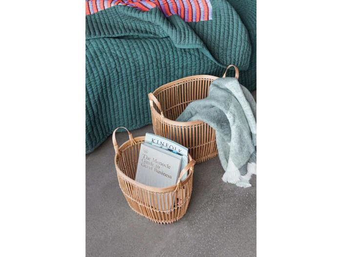 To flettede kurve på et gråt gulv, den ene med en bog og et magasin, den anden draperet med et grønt tæppe; et grønt quiltet sengetæppe i baggrunden.