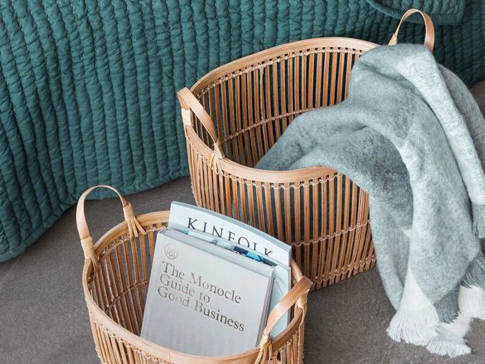 To flettede kurve på gulvet, den ene med et foldet grønt og hvidt tæppe, den anden med bøger og magasiner. Et struktureret grønt tæppe ligger i baggrunden.