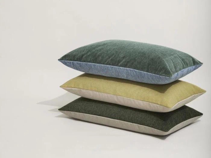 Tre rektangulære puder i grønne, gule og mørkegrønne farver er stablet oven på hinanden mod en almindelig hvid baggrund.