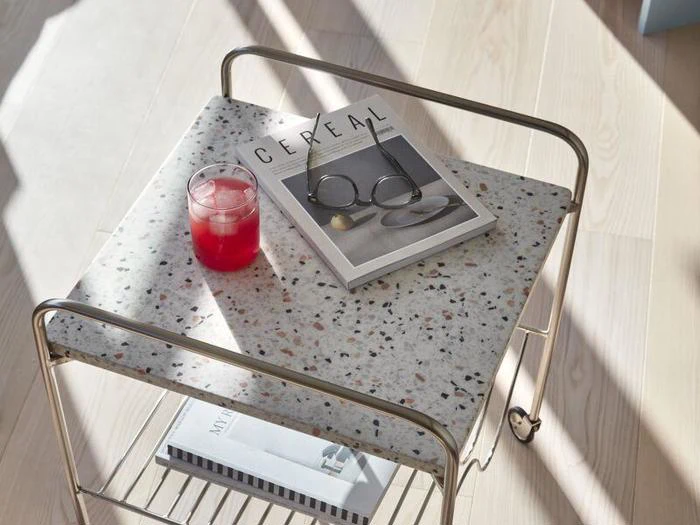 Et terrazzo-sidebord med en rød drink, briller og et Cereal-magasin på toppen, i sollys, på et lyst trægulv.