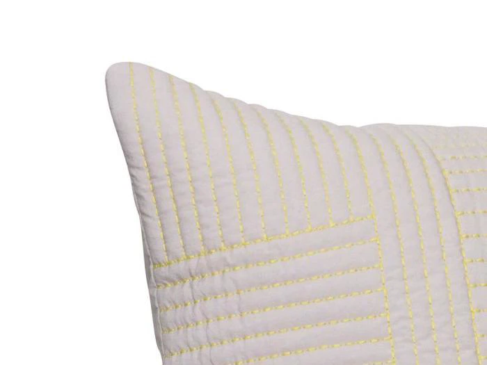 Nærbillede af hjørnet af en hvid quiltet pude med gule syninger i et lineært mønster.