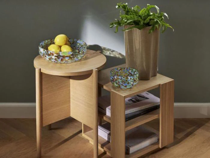 To redeborde i træ med en glasskål med citroner, en potteplante, en mindre glasskål og bøger stablet på den nederste hylde, op ad en væg.