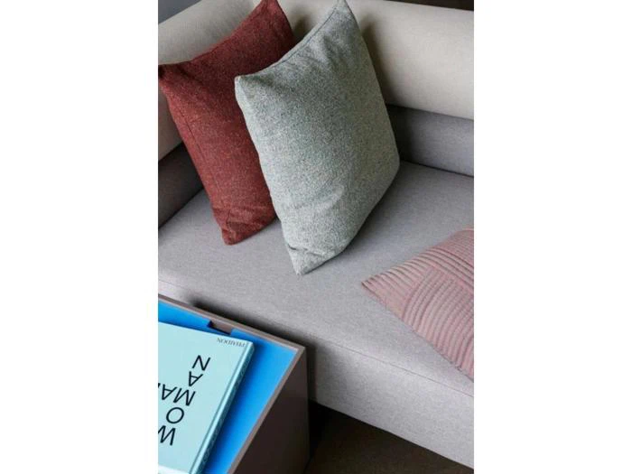 En lysegrå sofa med tre puder - en grå, en rød og en pinkstribet - ved siden af et sidebord med et blåt magasin.