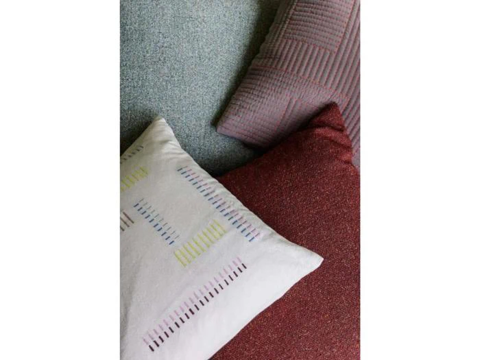 Tre puder overlapper hinanden: en lyseblå pude med struktur, en lyslilla pude med striber og en hvid pude med flerfarvede syninger samt en rød pude med struktur.