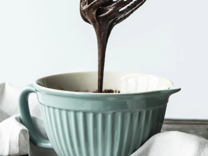 En blågrøn røreskål fyldt med chokoladedej med et piskeris, der er løftet op, så dejen drypper tilbage i skålen.